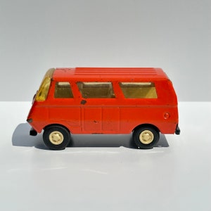 May include: A vintage toy red van with yellow windows. The van has black wheels with gold centers.