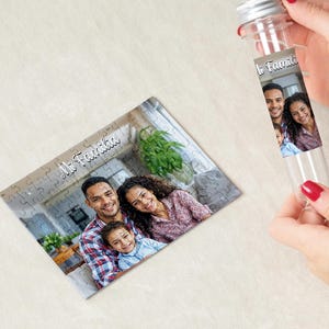 May include: A personalized family photo puzzle and a clear tube with a silver cap, also featuring a family photo. The puzzle is partially assembled, displaying a smiling family. The tube has a photo label with the family's image.