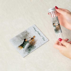 May include: A clear glass tube with a silver cap and a watercolor image of a father and child. A completed jigsaw puzzle with the same image and the text "Happy Father's Day" is next to the tube.