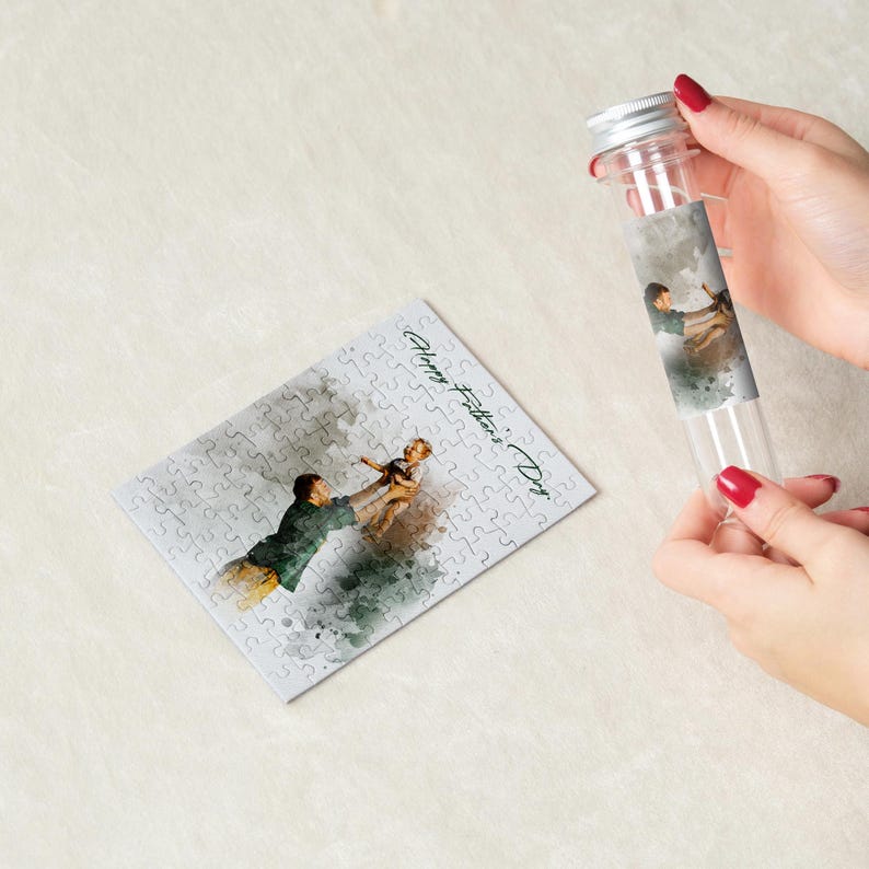 May include: A clear glass tube with a silver cap and a watercolor image of a father and child. A completed jigsaw puzzle with the same image and the text "Happy Father's Day" is next to the tube.
