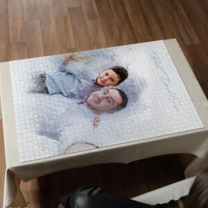 May include: A personalized jigsaw puzzle featuring a photograph of a man and a child. The puzzle is mostly white with a light-colored border and is displayed on a beige tablecloth. The image shows the faces of the man and child.