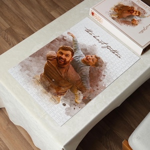 May include: A 500-piece jigsaw puzzle featuring a watercolor-style image of a father and child. The puzzle is mostly white with the words "the best father" in cursive. The puzzle box is visible in the upper right corner.