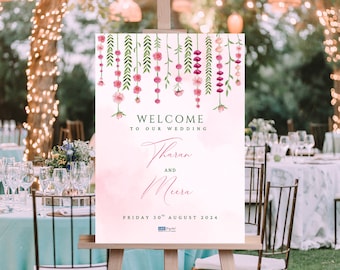 May include: A wedding welcome sign on an easel. The sign has a watercolor design with pink flowers and green leaves. The text reads "WELCOME TO OUR WEDDING" and the names "Tharan and Meera" with the date "FRIDAY 30th AUGUST 2024".
