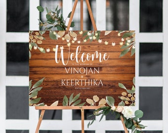 May include: Welcome sign with a rustic wood background, greenery, and string lights. The sign reads "Welcome to the wedding of Vinojan & Keerthika 31st October 2021".