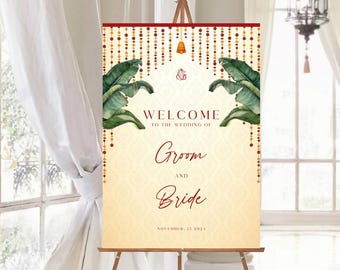May include: A wedding welcome sign on a wooden easel. The sign features the words "Welcome to the Wedding of Groom and Bride" in burgundy script, with green banana leaves and gold accents. The date is November 15, 2024.