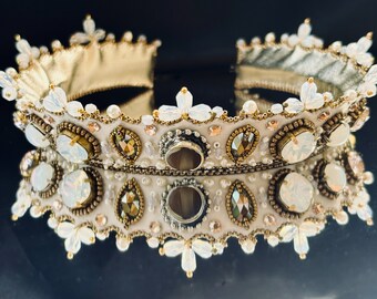 Könnte beinhalten: Eine weiße und goldene Perlenkrone mit floralem Design. Die Krone ist mit schillernden Steinen und Perlen verziert.