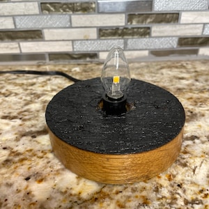 May include: A small wooden lamp base with a black finish and a clear light bulb. The base is made from reclaimed wood and has a rustic look.