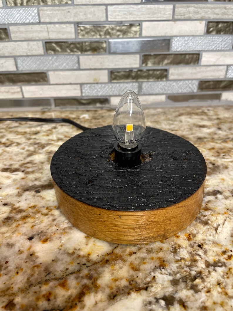 May include: A small wooden lamp base with a black finish and a clear light bulb. The base is made from reclaimed wood and has a rustic look.