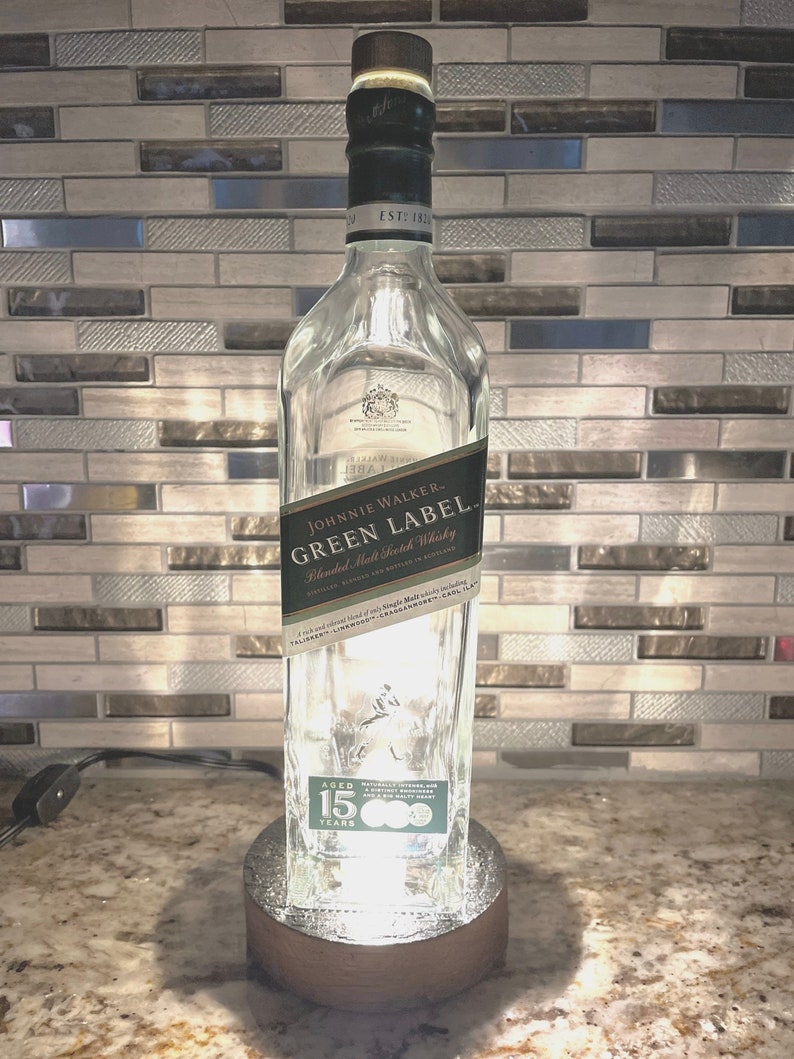 May include: A clear glass bottle with a green label that reads "JOHNNIE WALKER. GREEN LABEL. Blended Malt Scotch Whisky" and "AGED 15 YEARS". The bottle is sitting on a wooden base.