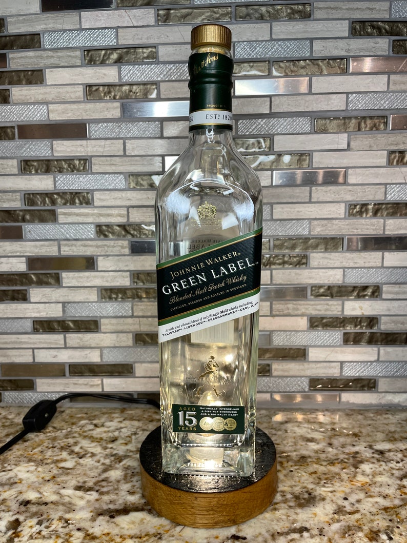 May include: A clear glass bottle with a green label that reads "Johnnie Walker Green Label Blended Malt Scotch Whisky" and "Aged 15 Years". The bottle is sitting on a wooden base.