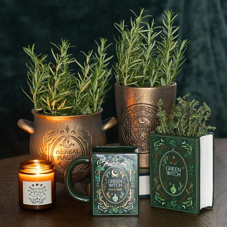 Herbal Magic Kräutertopf im Kessel-Design aus Terrakotta mit Rosmarin, dekoriert mit Kerze und Green Witch Tasse auf Holztisch