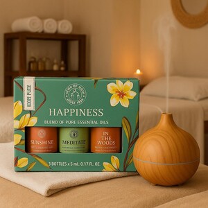 Könnte beinhalten: Eine grüne Box mit dem Wort "HAPPINESS" und drei ätherischen Ölflaschen: "SUNSHINE", "MEDITATE" und "IN THE WOODS". Ein ätherischer Öl-Diffusor aus Holz befindet sich neben der Box. Die Box hat ein Blumenmuster.