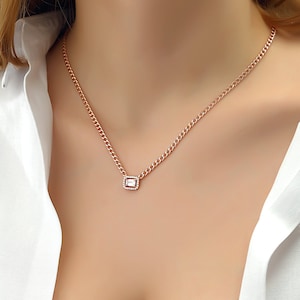 Op de afbeelding: Een ketting van roségoud met een klein vierkant hanger met een heldere, gefacetteerde edelsteen omringd door kleinere stenen.