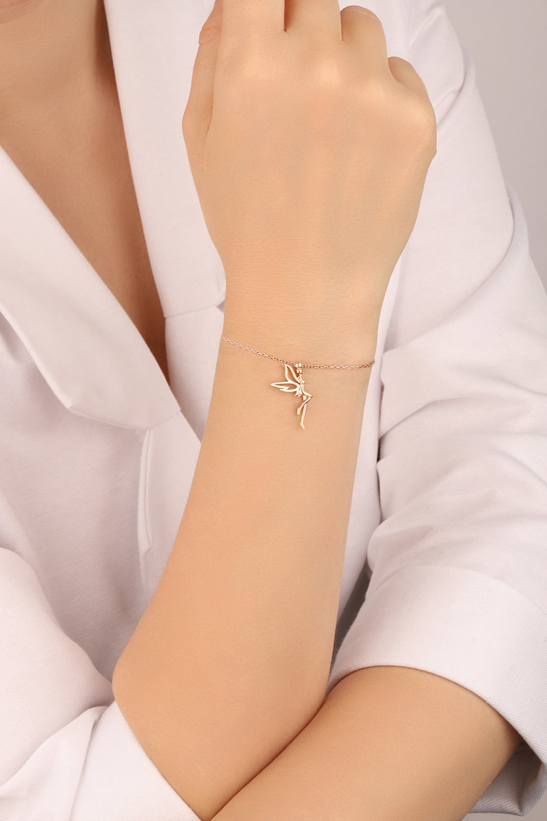 Puede incluir: Un delicado brazalete de oro con un dije de hada. El brazalete est&aacute; hecho de una cadena fina y el dije de hada es detallado e intrincado.