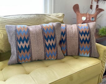 May include: Two rectangular throw pillows with a brown and gray woven fabric. Each pillow features a central vertical stripe with a blue and tan zigzag pattern. The pillows are resting on a yellow-green sofa.