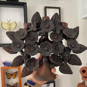 May include: A dark brown, matte-finished clay candelabra featuring a central stem that branches out into multiple sculpted flowers and leaves. The decorative piece includes small bird figures perched among the floral elements and three candle holders.