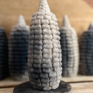 Puede incluir: Un conjunto de cinco candelabros de maíz de cerámica gris y negro. Los candelabros están dispuestos en una fila sobre una superficie de madera.
