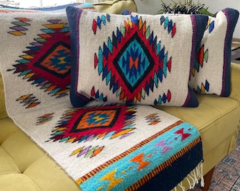 May include: A set of three throw pillows with a white background and colorful geometric patterns. The pillows are on a green couch with a matching throw blanket.