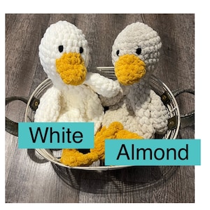 May include: Two crocheted plush duck toys in a wire basket. One duck is white and the other is almond colored. Both ducks have yellow beaks and feet.