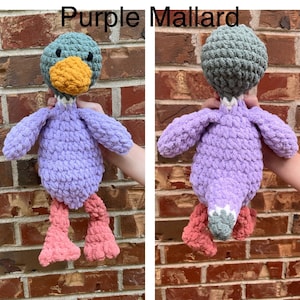May include: Purple crocheted mallard duck plush toy with a green head and orange beak. The duck has pink legs and a white stripe around its neck.