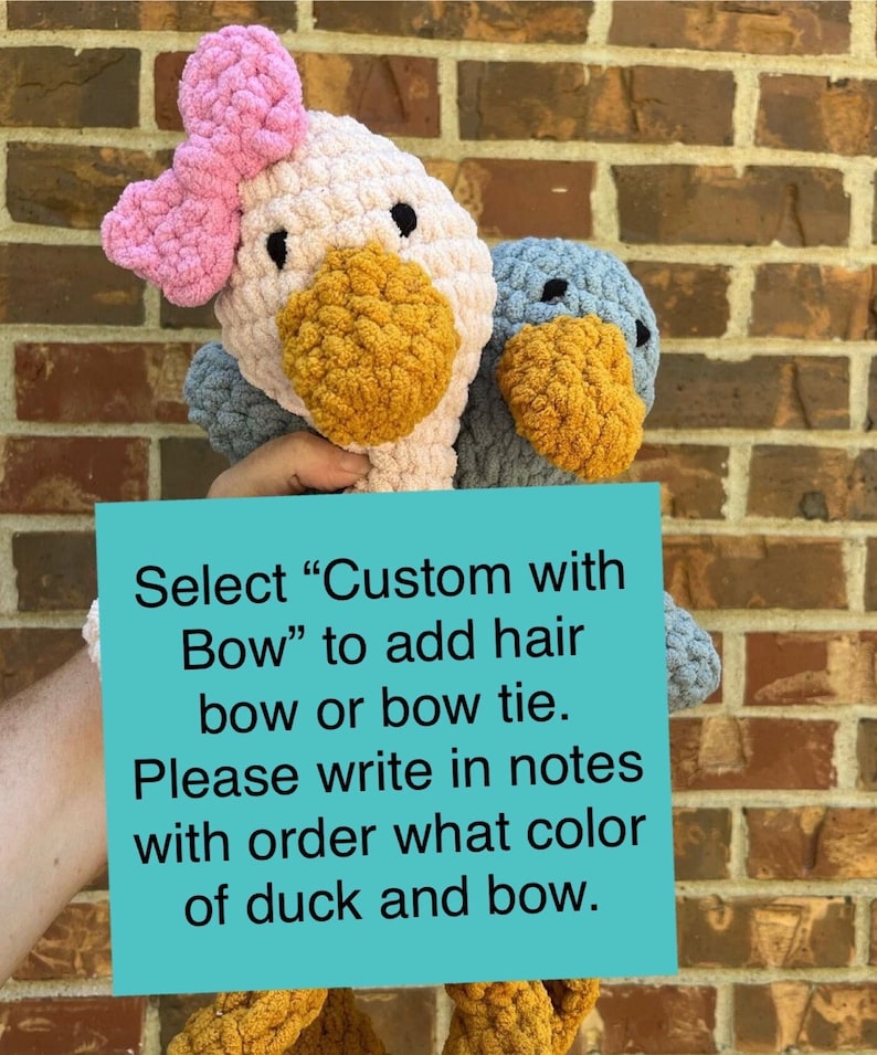 May include: Two crocheted duck plushies, one with a pink bow. The sign reads "Select "Custom with Bow" to add hair bow or bow tie. Please write in notes with order what color of duck and bow."