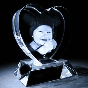 Puede incluir: Un pisapapeles de cristal con forma de coraz&oacute;n con una imagen grabada en 3D de un beb&eacute; con un sombrero. El coraz&oacute;n est&aacute; sobre una base de cristal transparente.
