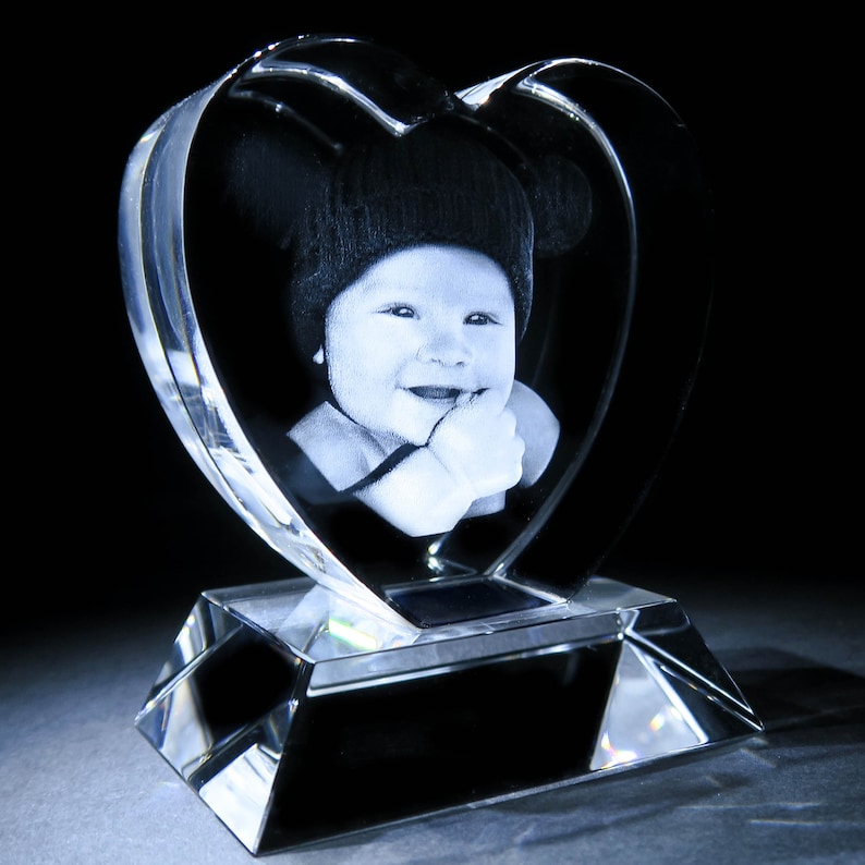 Puede incluir: Un pisapapeles de cristal con forma de coraz&oacute;n con una imagen grabada en 3D de un beb&eacute; con un sombrero. El coraz&oacute;n est&aacute; sobre una base de cristal transparente.