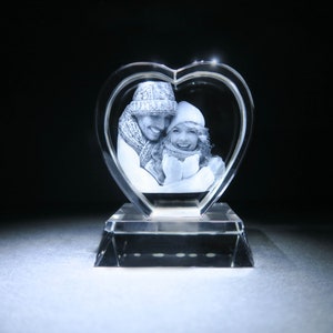Puede incluir: Un pisapapeles de cristal en forma de coraz&oacute;n con una imagen grabada en 3D de una pareja con ropa de invierno.