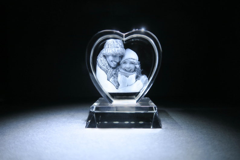 Puede incluir: Un pisapapeles de cristal en forma de coraz&oacute;n con una imagen grabada en 3D de una pareja con ropa de invierno.