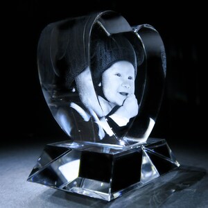Puede incluir: Un pisapapeles de cristal en forma de coraz&oacute;n con una imagen grabada en 3D con l&aacute;ser de un ni&ntilde;o con un sombrero. El pisapapeles est&aacute; sobre una base de cristal transparente.