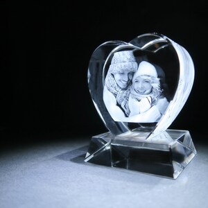 Puede incluir: Un pisapapeles de cristal en forma de coraz&oacute;n con una imagen grabada en 3D de una pareja con ropa de invierno.