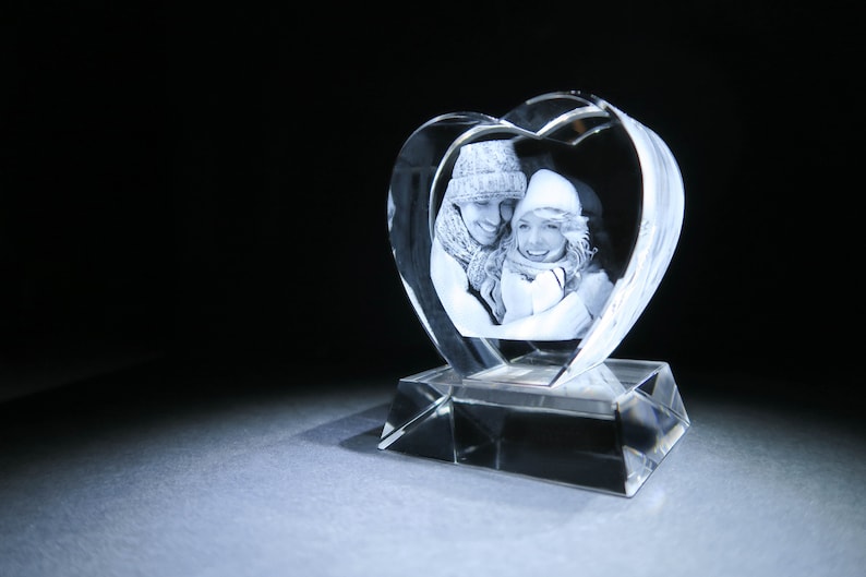 Puede incluir: Un pisapapeles de cristal en forma de coraz&oacute;n con una imagen grabada en 3D de una pareja con ropa de invierno.