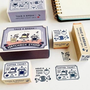 May include: A set of six wooden rubber stamps with various designs. The stamps feature illustrations of coffee, lemonade, candy, and text that says "Take a Break!" and "Have a Good Time!" The stamps are packaged in small wooden boxes.
