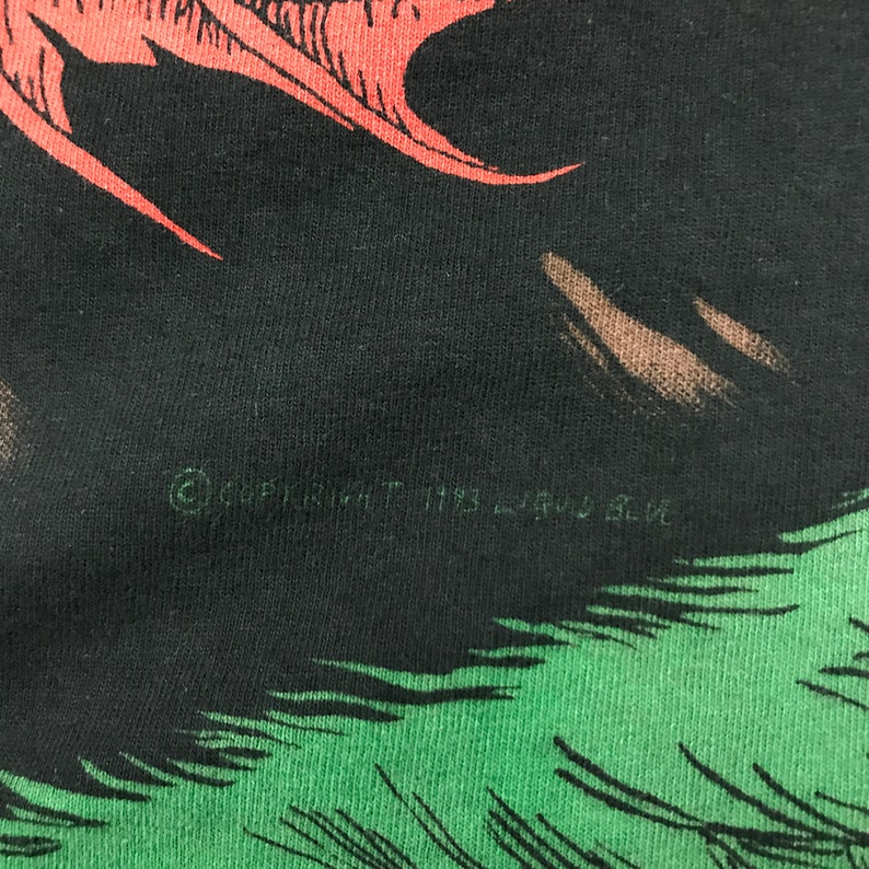 May include: Black t-shirt with a green and red graphic print of a creature. The text "Copyright 1993 Land Shark" is printed on the shirt.