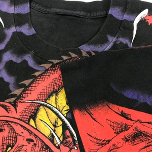May include: Black t-shirt featuring a red, yellow and white dragon graphic print. The dragon has sharp claws and teeth. The shirt has a distressed look.