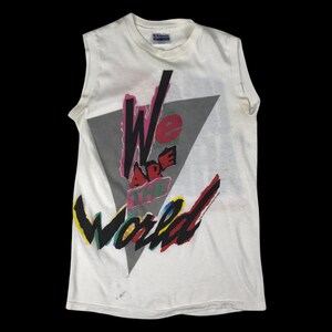 May include: White sleeveless t-shirt with a graphic print of the words "We Are The World" in a colorful, geometric design.