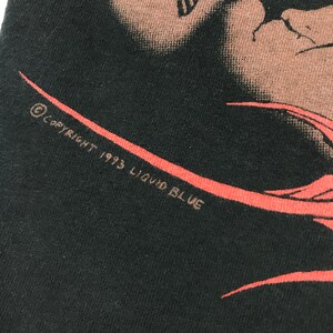 May include: Black t-shirt with a red and white graphic design. The text "Copyright 1993 Liquid Blue" is printed on the bottom of the shirt.