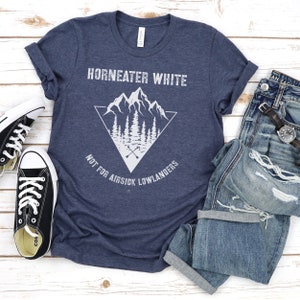 May include: A navy blue t-shirt with a white graphic design of a mountain range inside a triangle with the text "Horneater White Not For Airsick Lowlanders".