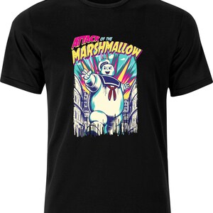 以下が含まれることがあります： 黒いTシャツに、白いマシュマロの幽霊のグラフィックが描かれており、ピンク、青、黄色の「Attack of the Marshmallow」という文字が書かれています。