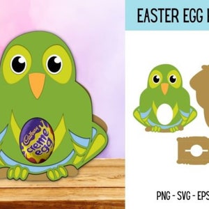 Puede incluir: Porta huevos de Pascua en forma de b&uacute;ho verde con un dise&ntilde;o azul y amarillo. El porta huevos tiene un agujero en el centro para sostener un huevo. El porta huevos est&aacute; sentado sobre una superficie de madera. El texto "EASTER EGG HOLDER" est&aacute; en la parte superior de la imagen.