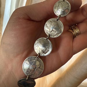 May include: A silver bracelet made from linked US coins. The coins feature the profiles of Liberty, the American Buffalo, and the Statue of Liberty.