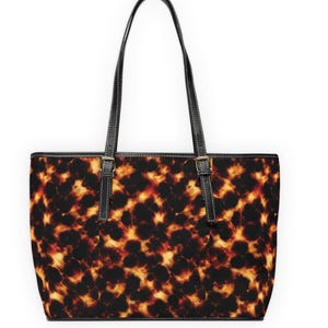 May include: A tote bag with a tortoiseshell pattern in shades of brown, black, and yellow. The bag has black handles and trim with silver-colored buckles. The bag is designed for carrying items.