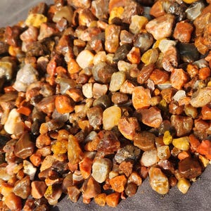 Puede incluir: Primer plano de un montón de pequeñas piedras de ágata de colores. Las piedras son principalmente de color marrón, rojo y amarillo.