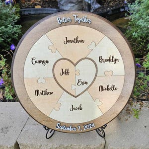 May include: A wooden puzzle with the words "Better Together" and names like Jonathan, Brooklyn, and Jeff. The puzzle is round with a heart-shaped center and the date "September 7, 2024" at the bottom. The puzzle is displayed on a black metal stand.