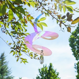 May include: A iridescent pink and blue spiral wind chime with a crystal prism hanging from the bottom. The chime is hanging from a tree branch.