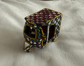 Könnte beinhalten: Ein dekorativer, miniaturisierter Auto-Rikscha mit schwarzer Basis, verziert mit Spiegelfliesen, roten und silbernen Akzenten und gelben Zierleisten. Das Dach hat ein Schachbrettmuster. Die Räder sind goldfarben. Der Innenraum ist rot.
