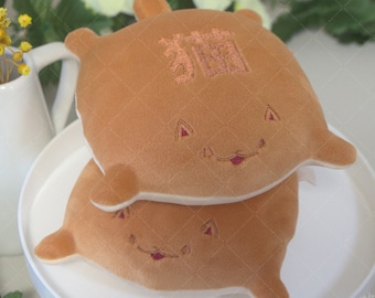 May include: Two brown plush toys shaped like a Shiba Inu dog, stacked on top of each other on a white plate. The top toy has the Japanese character for "dog" embroidered on its back.
