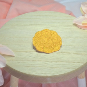 May include: A yellow embroidered patch with Chinese characters on a light wood surface. The patch is round and has a raised design.