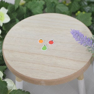 May include: Three embroidered iron-on patches of fruit: an orange, an apple, and a pear. The patches are on a light wood surface.