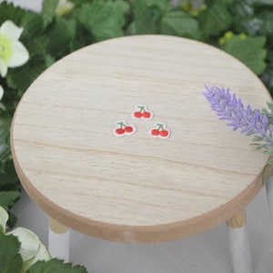 May include: Four red cherry stickers on a light brown wooden round table top.